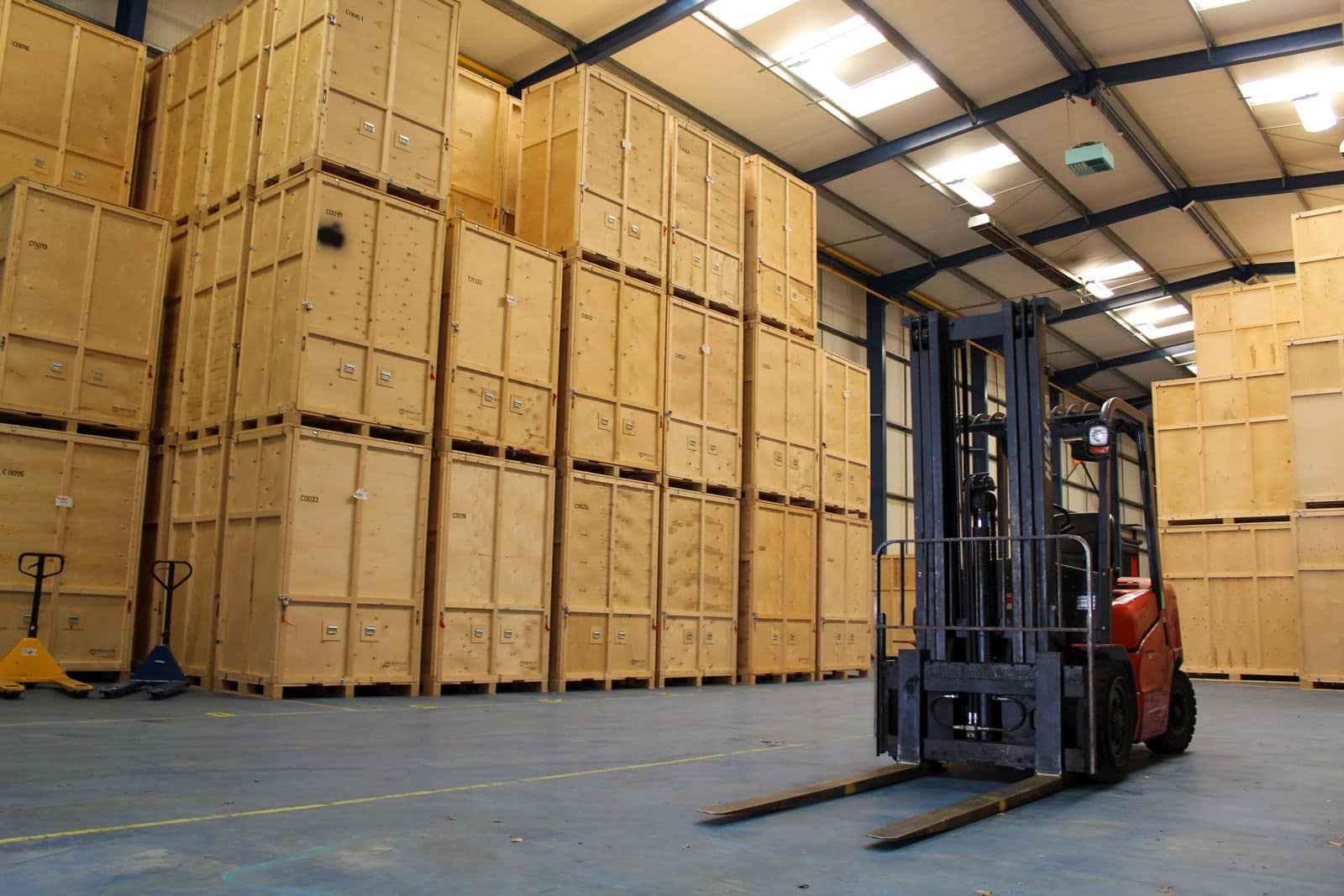 Forklift parked between rows of wooden storage crates inside Henfield’s warehouse
