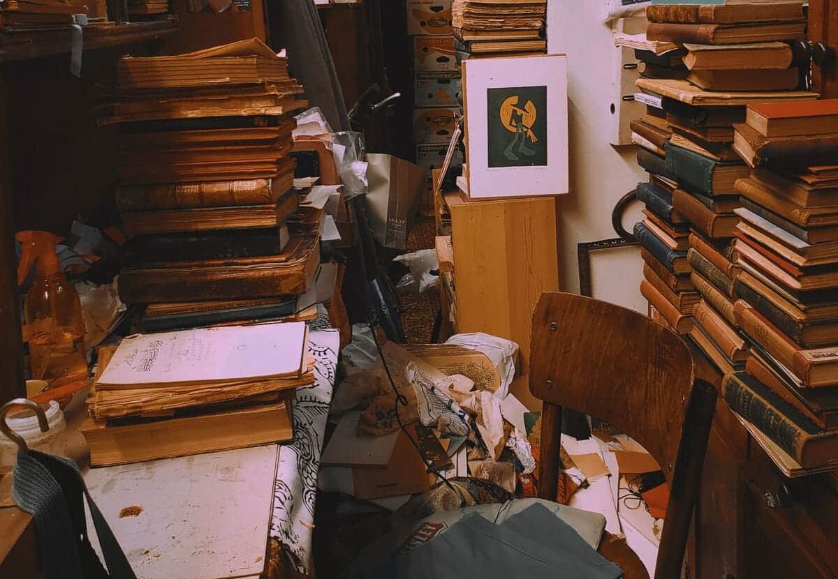 a messy study, stacks of books and other items