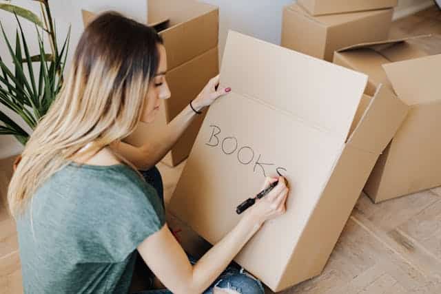 Woman writing on a cardboard box while packing books for self storage